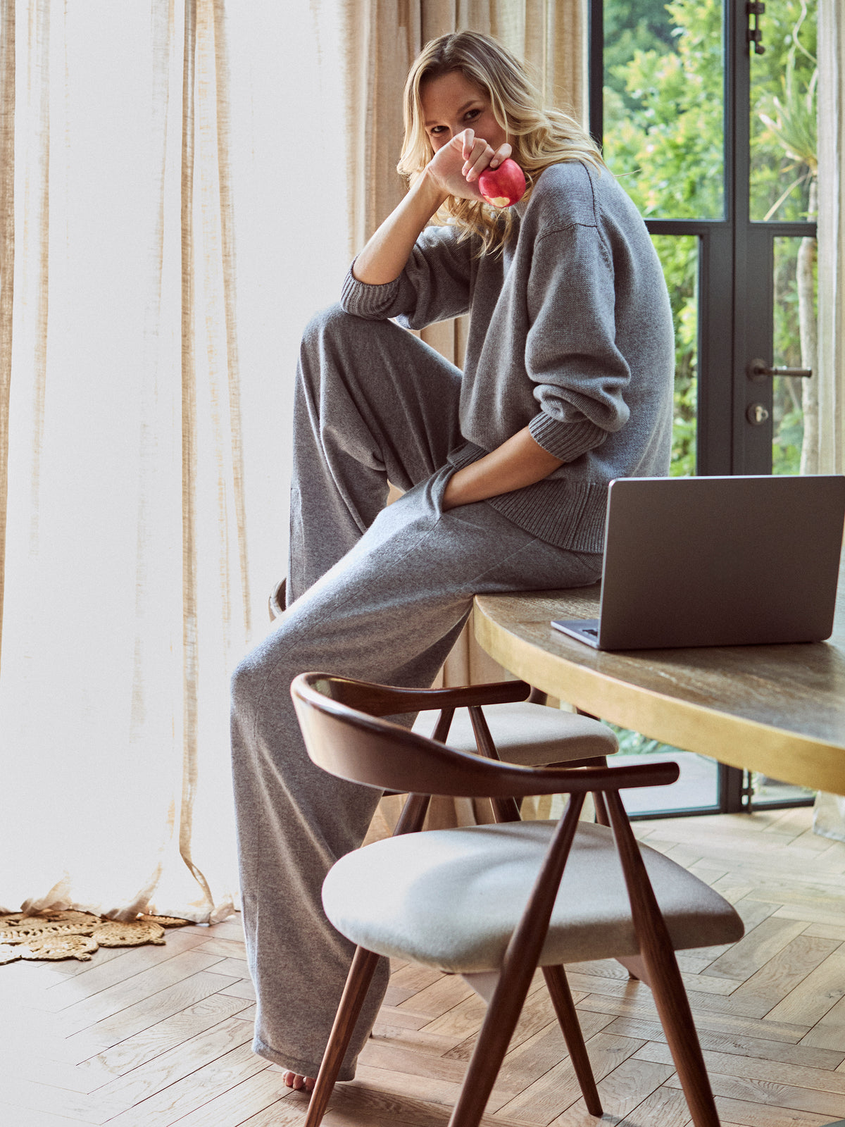 Model wearing Laffue cashmere jumper and trousers whilst sitting on a table.